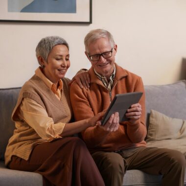 Man and Woman Sitting on Sofa While Looking at a Tablet Computer