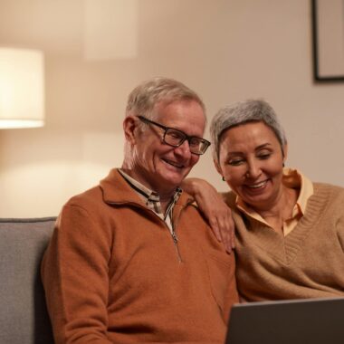 Man and Woman Sitting on Sofa While Looking at a Laptop